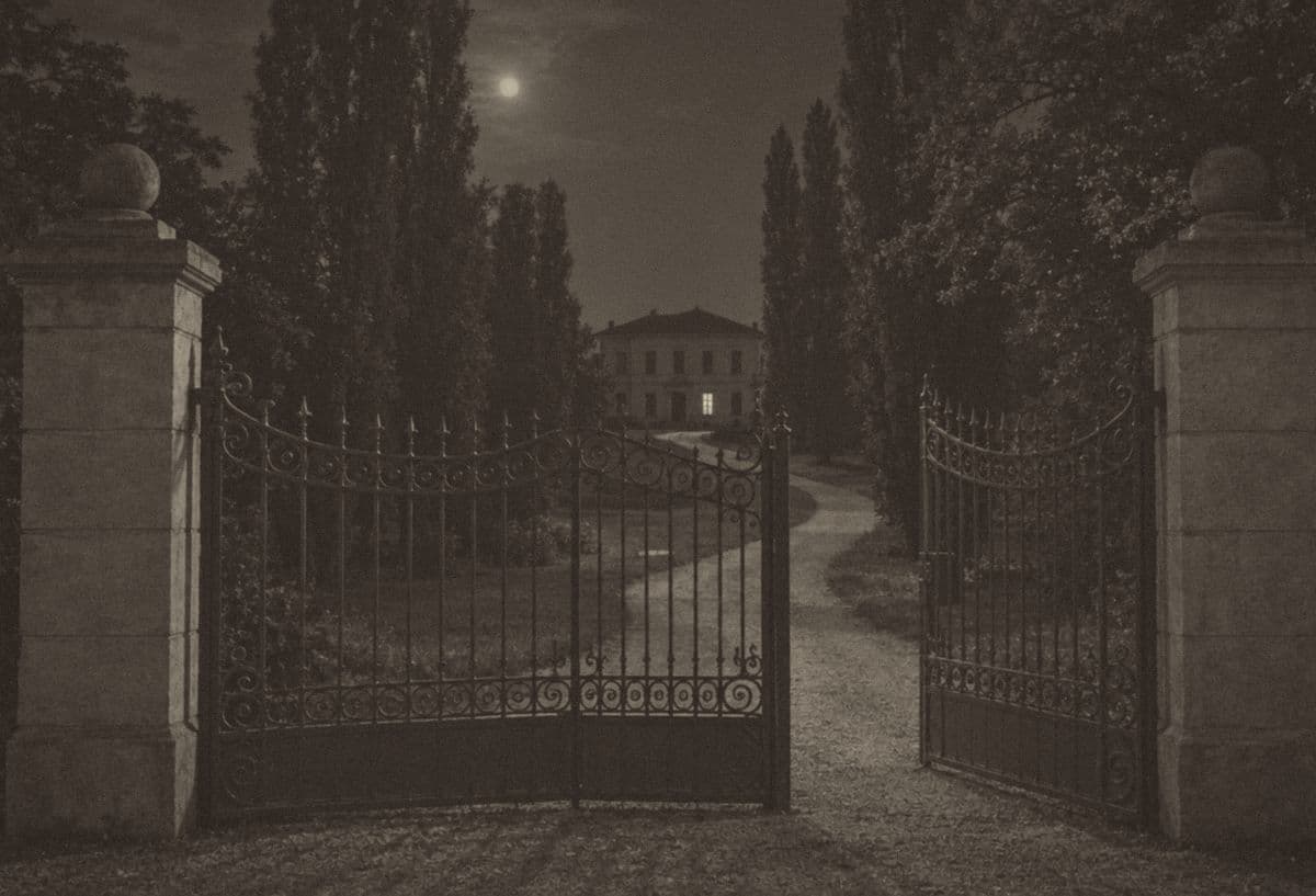 Stara crno-bela fotografija noću: otvorena kovana kapija, prilaz kroz drveće i u daljini vila sa jednim osvetljenim prozorom u prizemlju